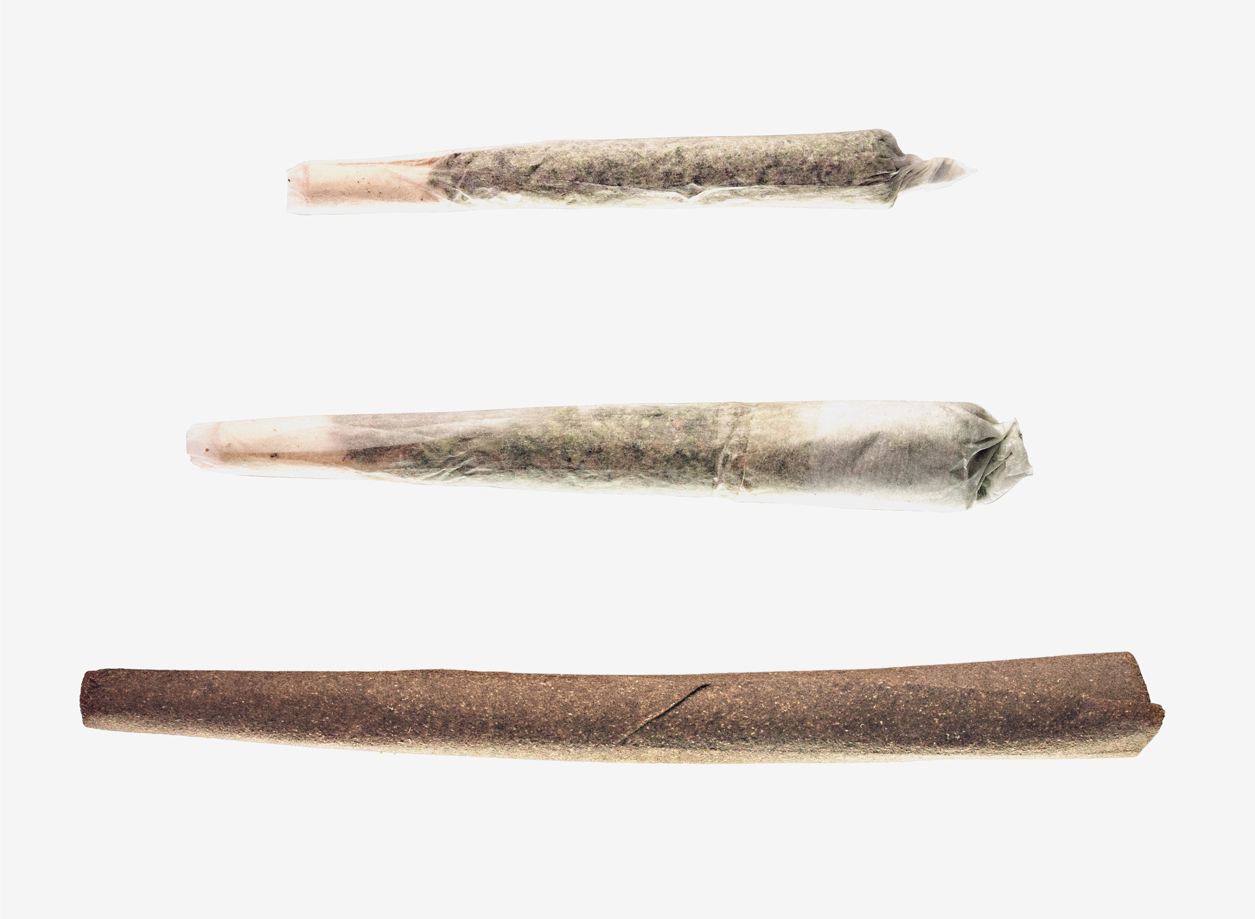 Three hand-rolled joints of varying paper types laid horizontally on white background