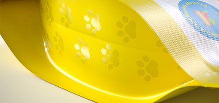 Glossy yellow flexible packaging with paw print patterns, designed for pet products with vibrant and playful branding.